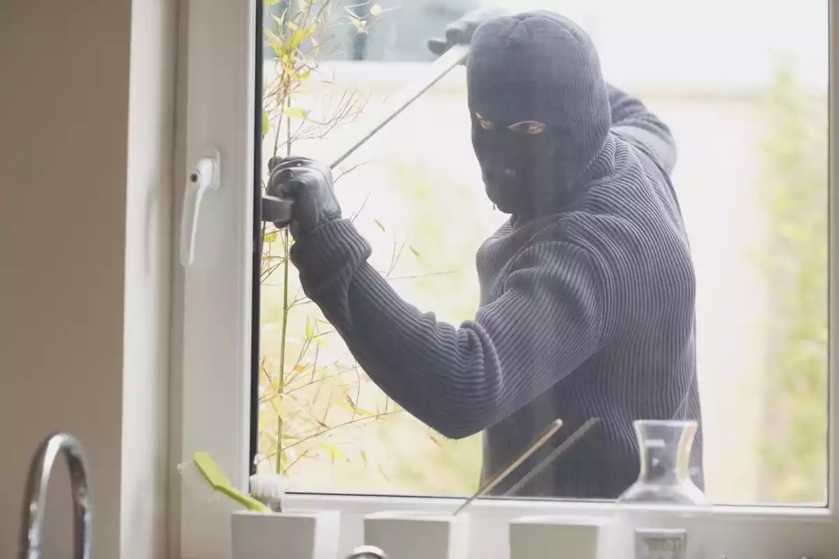 Ladrón encapuchado intentando forzar una ventana
