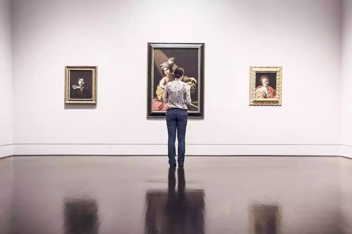 Una mujer ante 3 cuadros en una sala de exposiciones